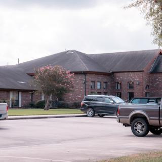 A brick building with a parking lot and several vehicles on a cloudy day.