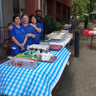 A group of people in blue shirts gathered around a table filled with food at an outdoor event.