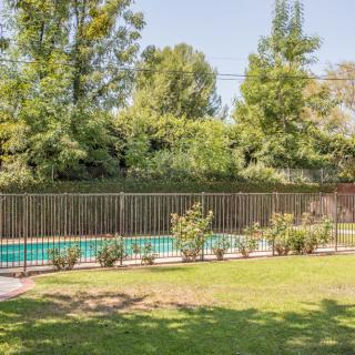 A fenced swimming pool surrounded by a garden with trees.
