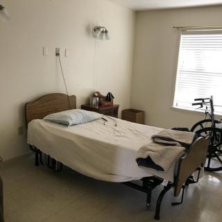 A hospital room with a bed and wheelchair, featuring medical equipment and a window letting in natural light.