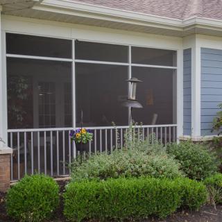 A screened porch with a garden view, featuring shrubs and a bird feeder.