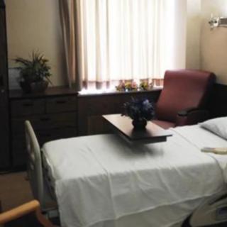 A neatly arranged hospital room with a bed, side table, and chair near a window.