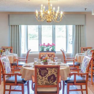 An elegant dining room with beautifully set tables and a chandelier, featuring large windows for natural light.