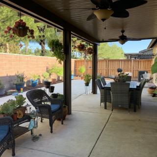 A cozy patio with outdoor seating and a dining area, surrounded by plants and hanging baskets.