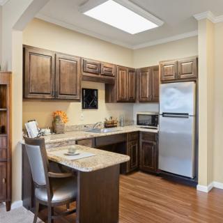 A modern kitchen with wooden cabinets and flooring, featuring a refrigerator and small dining area.