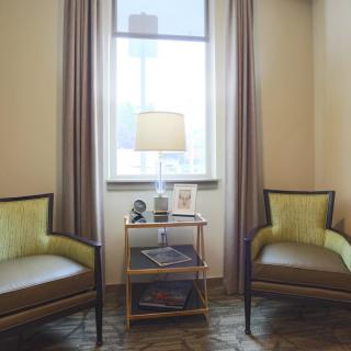 A cozy sitting area with two chairs, a lamp on a small table, and a window with curtains.