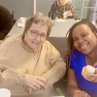 Two people smiling while sitting at a table indoors.