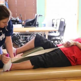 A healthcare professional assists a patient with physical therapy exercises.