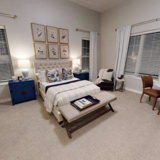 A cozy, well-decorated bedroom with a neatly arranged bed, artwork on the wall, and warm lighting.