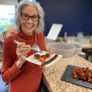 A smiling woman with glasses holding a plate of food in a kitchen.
