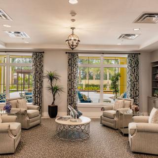 A cozy living room with comfortable seating, elegant chandelier, and large windows with patterned curtains.