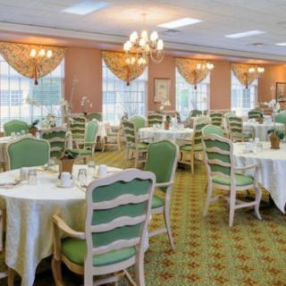 An elegantly decorated dining room with multiple tables and chairs, featuring chandeliers and large windows.