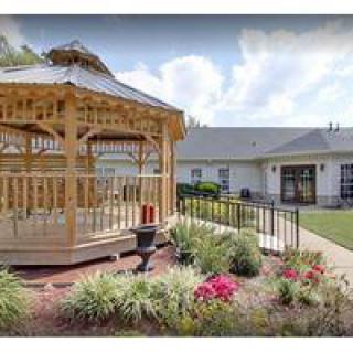A beautifully landscaped garden featuring a wooden gazebo and vibrant flowers in front of a building.