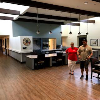 A spacious interior with two individuals walking through a modern lobby featuring a kitchenette area.