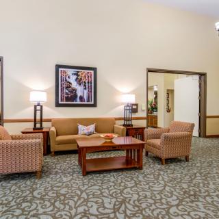A cozy lobby seating area with sofas, chairs, and a central table, complemented by lamps and artwork on the wall.