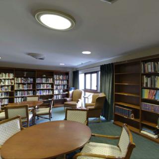 A cozy library room with bookshelves, tables, and chairs for reading.