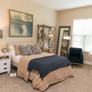A cozy and modern bedroom with a neatly made bed, decorative pillows, and an elegant shelving unit beside a floor-length mirror.