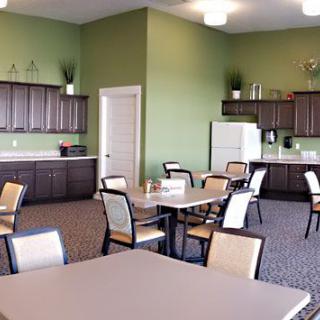 A modern dining area with tables and chairs, featuring a kitchenette against green walls.