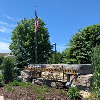 A park sculpture with an American flag surrounded by greenery on a sunny day.