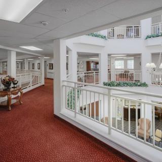 A spacious modern hallway overlooking an atrium with white railings and red carpeting.