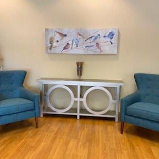 A stylish living room with two blue armchairs and a white console table beneath abstract artwork.