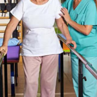A healthcare professional assists an elderly person with physical therapy using parallel bars.