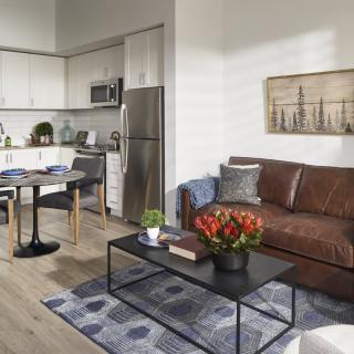 A modern apartment featuring a cozy living room with a brown leather sofa and a stylish kitchen in the background.