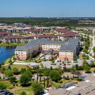 Aerial view of a residential area featuring apartment buildings, a lake, and surrounding greenery.