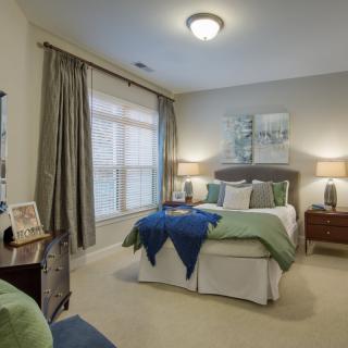 A cozy bedroom with a neatly made bed, two bedside lamps, and large windows with curtains.