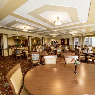 A spacious dining area with neatly arranged tables and chairs, featuring elegant lighting and a patterned carpet.