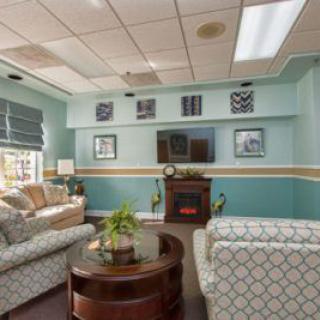 A cozy living room with patterned sofas, a central coffee table, and a wall-mounted TV above a fireplace.