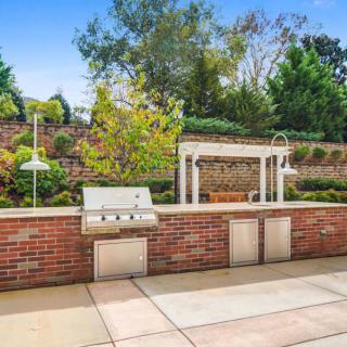 A well-designed outdoor kitchen with a brick grill and a pergola set in a landscaped garden.