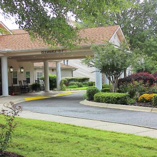 A building entrance with a landscaped driveway surrounded by trees, shrubs, and flowers.