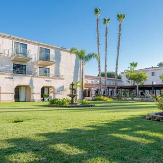 A hotel with a lush garden and palm trees on a sunny day.