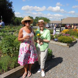 Two women enjoying a sunny day in the garden, wearing hats and holding flowers.
