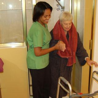 A caregiver assisting an elderly person with a walker.