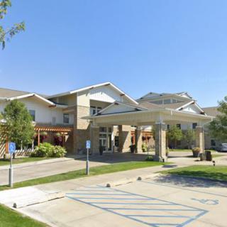 The exterior view of a modern building with a covered entrance and surrounding greenery, adjacent to a parking lot.