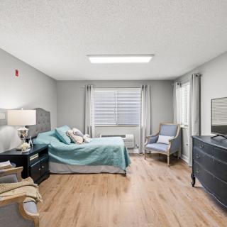 A modern and spacious bedroom with a bed, armchair, dresser, and large window.