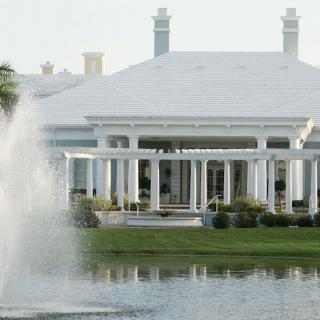 A grand building with white pillars overlooking a pond with a fountain.