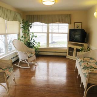 A cozy living room with a rocking chair and a TV, featuring large windows and wooden flooring.