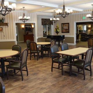 An elegant dining area with multiple tables and chairs, adorned with chandeliers and a piano in the corner.