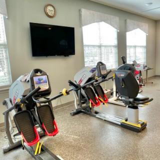 A well-lit gym with exercise machines and a television on the wall.