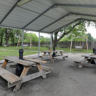 A spacious picnic area with wooden tables under a shelter, adjacent to a playground with swings.
