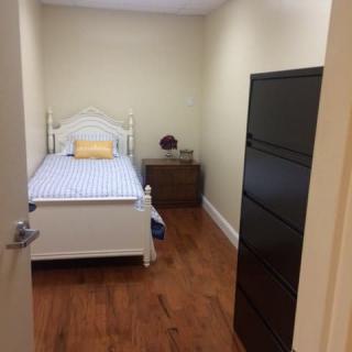 A small, minimalist bedroom with a single bed and a wooden dresser.