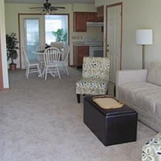 A cozy living room and dining area with modern furniture, including a sofa, patterned chairs, and a small brown table.
