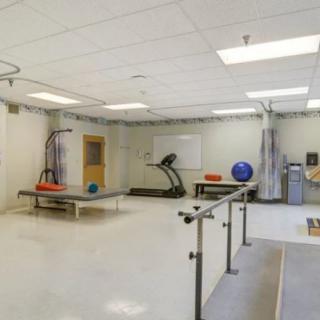 A spacious physical therapy room with various rehabilitation equipment, including a treadmill, parallel bars, and exercise balls.