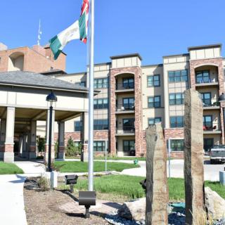 A modern residential apartment complex with a landscaped entrance and national flags flying in the foreground.