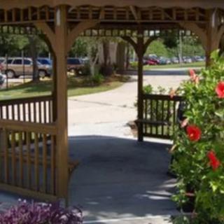 A wooden gazebo in a garden setting with vibrant red flowers and a walkway.