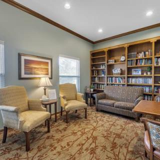 A cozy library room with a sofa, chairs, and a large bookshelf filled with books.