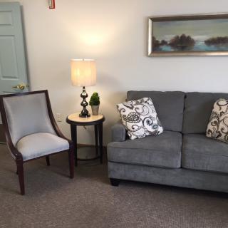A cozy living room with a gray sofa, an accent chair, a side table with a lamp, and wall art.